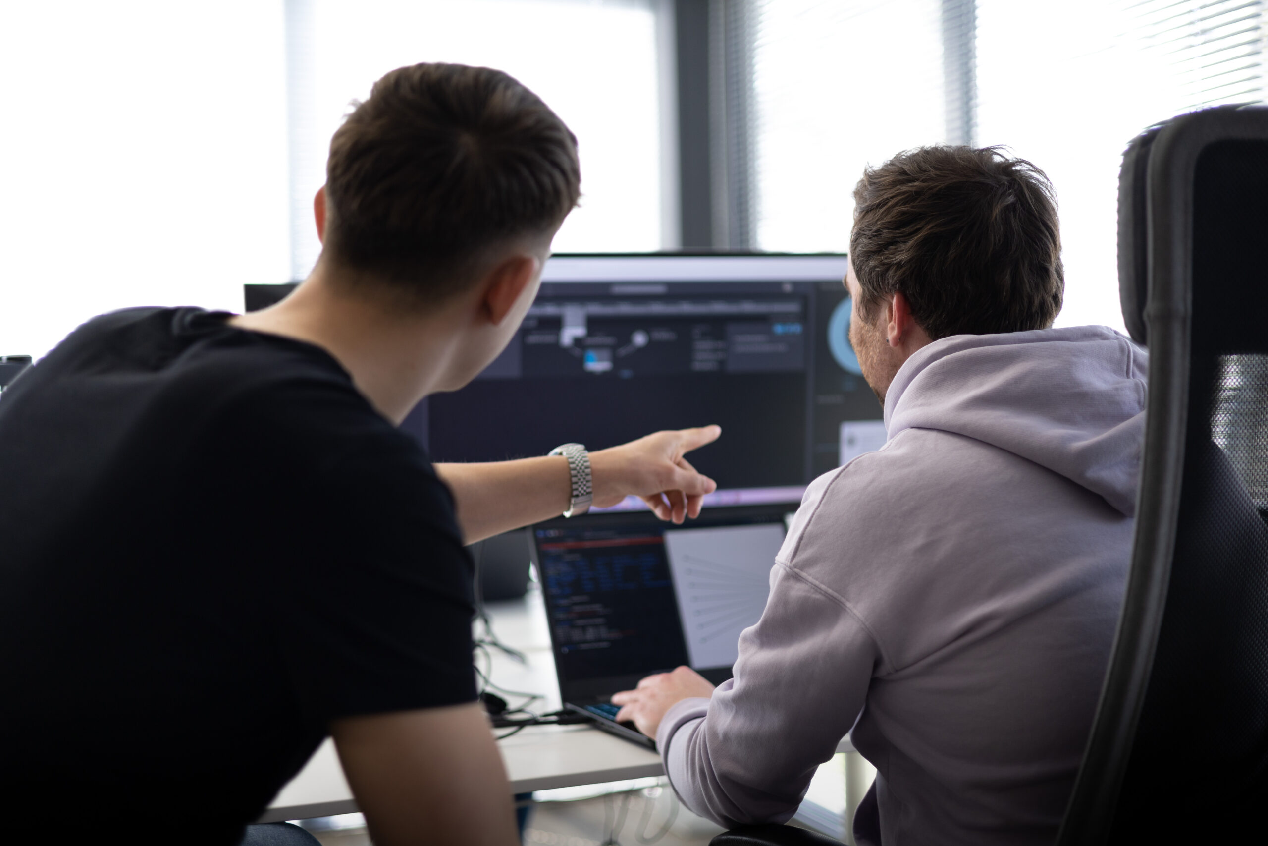 One analyst pointing at an alert dashboard while a colleague investigates on a laptop